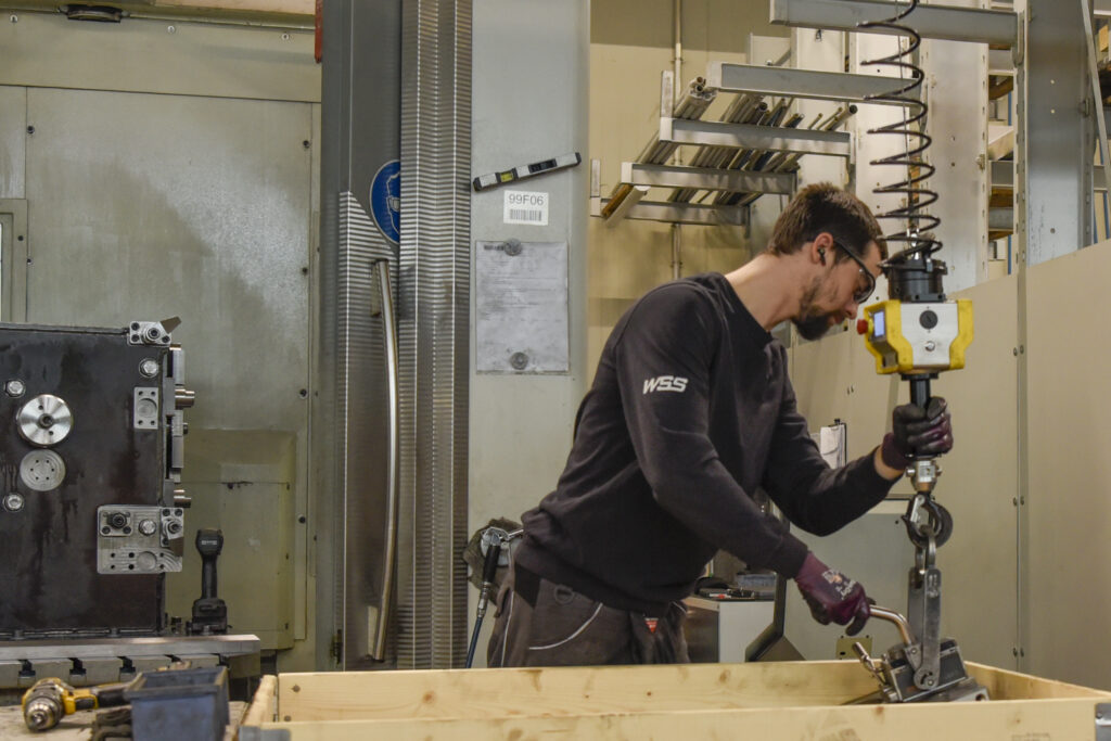 Mitarbeiter der WSS Metalltechnik hebt mithilfe einer Maschine schwerere Metallteile
