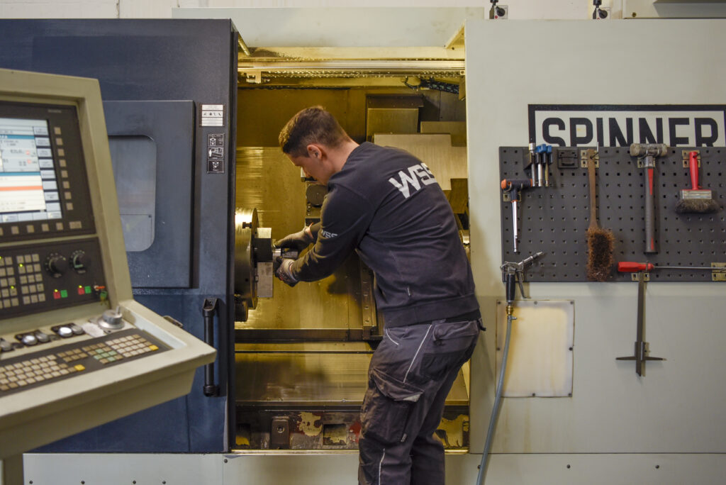 Mitarbeiter richtet Werkstück in CNC-Drehmaschine ein